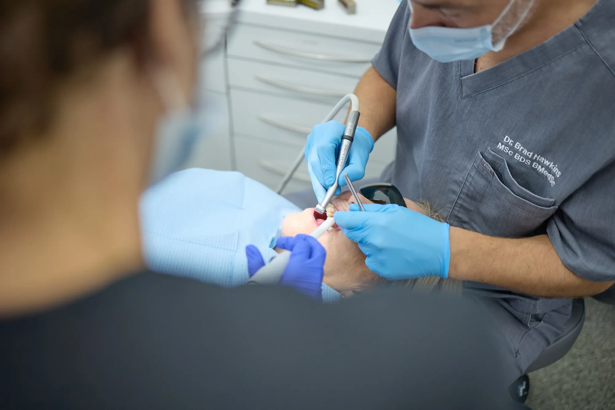 Dr Brad Hawkins carrying out implant treatment, viewed over the shoulder of an assisting nurse